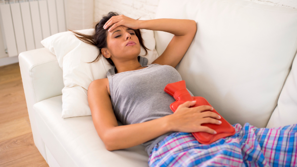A woman lying down with a hot water bottle holding her head in pain
